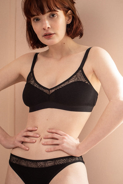 Une jeune femme se tient debout, les mains sur la taille et porte un ensemble de lingerie en coton biologique et dentelle recyclée.